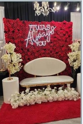 Red rose flower wall with neon sign, white loveseat and white floral arrangements