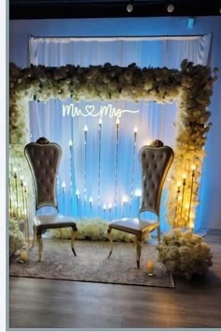 Evening ceremony arch with floral frame, glowing candles and throne chairs under blue uplighting
