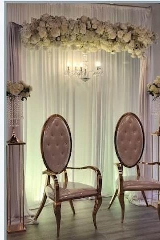 Ivory draped ceremony stage with floral garland, crystal chandelier and two tufted throne chairs, styled by Windsor Event Decor