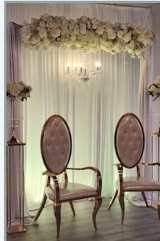 Ivory draped ceremony stage with floral garland, crystal chandelier and two tufted throne chairs, styled by Windsor Event Decor